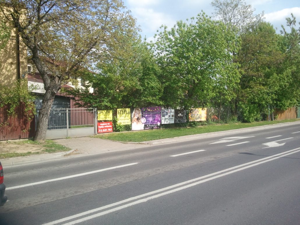 Na zdjęciu widzimy ogrodzenie posesji, na którym zawieszone są benery reklamowe. Zdjęcie wykonano w Piasecznie na ul. Gerbera